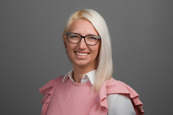 Ilgas Miezaines-Mustermanes portretfoto – sieviete ar platīnblondiem matiem, brilles tumšā rāmītī, rozā džemperī.